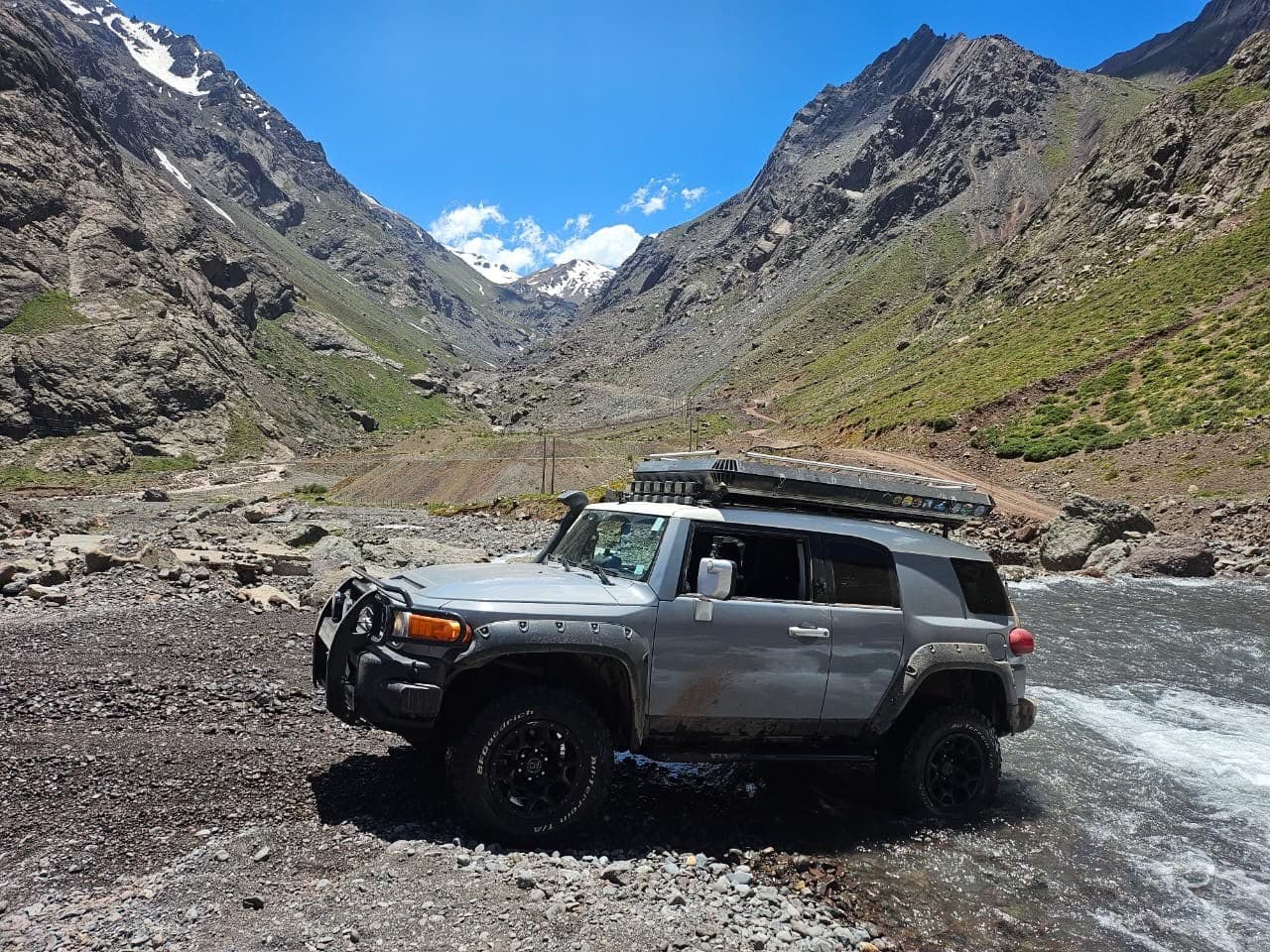 FJ Cruiser cruzando un río en la cordillera, rodeado de montañas nevadas